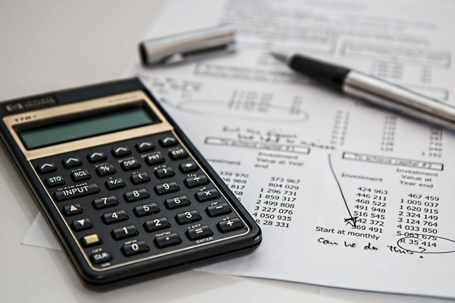 This picutre shows a calculator and a pen, and in the background an accounts sheet.
