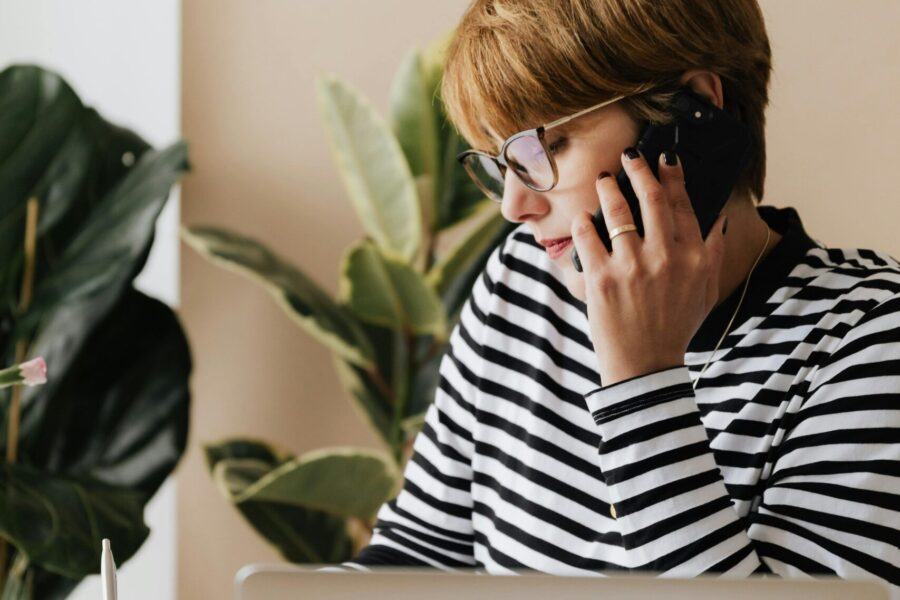 This picture shows a person on the a mobile phone, sat behind a desk with an apple laptop open in front of them
