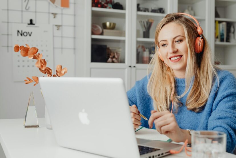 This picture shows a young woman with headphones on watching a laptop screen whilst sat at their desk